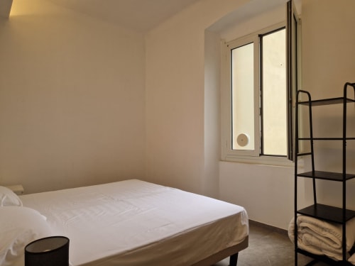 Camera da letto minimalista nell'appartamento di Genova con letto bianco, finestra con vista sulla città, scaffalature in metallo nero e pareti beige neutre