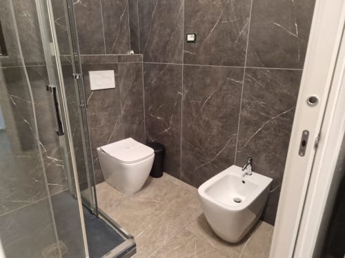 Bagno moderno nell'appartamento di Genova con rivestimento in marmo, toilet bianco, bidet e cabina doccia
