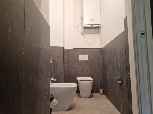 Bagno moderno dell'appartamento ML White House Genova con pareti in marmo scuro, sanitari bianchi, bidet, wc e scaldasalviette
