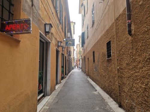 Stretto vicolo acciottolato a Genova con edifici in cotto, negozi e insegna neon FRESIA HOUSE