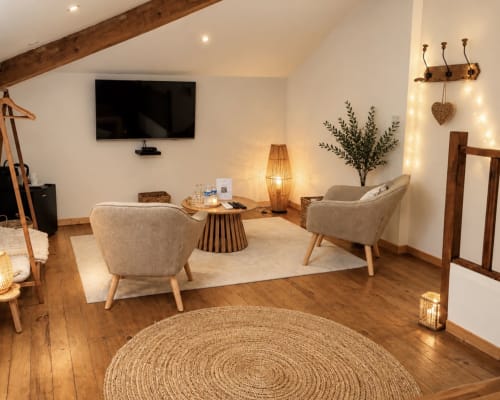 Cozy living area at Le Jardin d'Elusa Suite Marquèze with beige armchairs, wooden beams, and warm lighting
