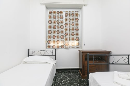 Due letti gemelli con biancheria bianca in Gelsomino House a Genova, con rivestimento finestra decorato e cassettiera in legno