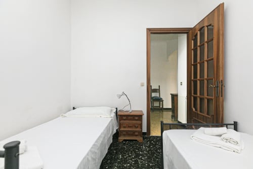 Camera da letto in appartamento Gelsomino House, Genova: due letti con biancheria bianca, comodino in legno, specchio e accesso alla vista della città.
