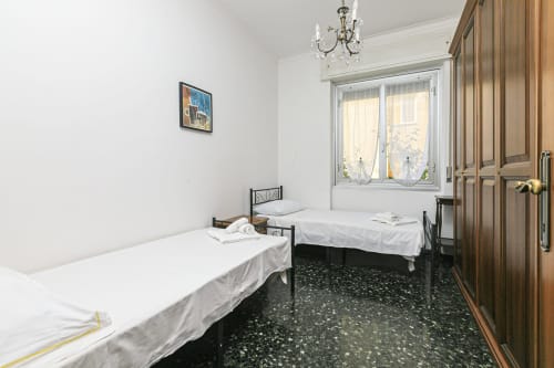 Camera doppia nella casa Gelsomino a Genova, con letti bianchi, pavimento in terrazzo e vista sulla città dalla finestra