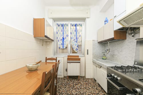 Cucina e zona pranzo moderna nell'appartamento Gelsomino House a Genova. Tavolo in legno con sedie, fornello a gas, rivestimento in marmo.
