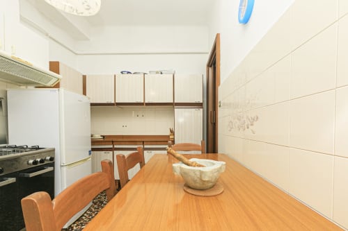 Moderna cucina e zona pranzo dell'appartamento Gelsomino House a Genova, con tavolo in legno, elettrodomestici attrezzati e rivestimenti in piastrelle color crema