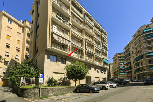 Edificio residenziale GELSOMINO HOUSE a Genova con freccia rossa che indica l'ubicazione dell'unità, auto parcheggiate e vista sulla città