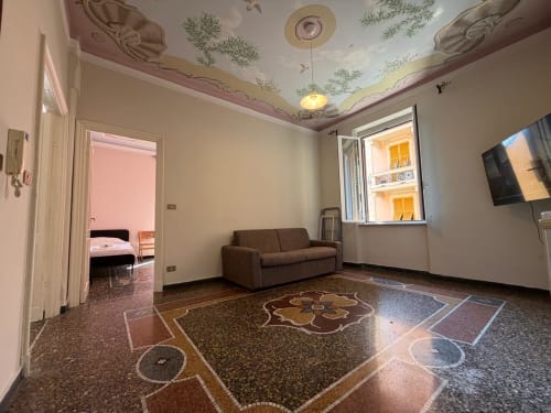 Salotto Tulipano House a Genova con pavimento in terrazzo decorativo, divano marrone, vista sulla città e affreschi ornamentali al soffitto