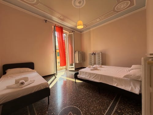 Camera da letto Tulipano a Genova con due letti, soffitto decorativo, tende rosse e accesso balcone con vista sulla città