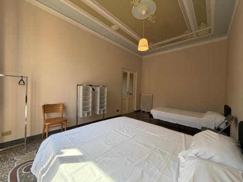 Ampia camera da letto nella Casa Tulipano, appartamento a Genova con più letti, dettagli classici al soffitto, sedia in legno e bianco