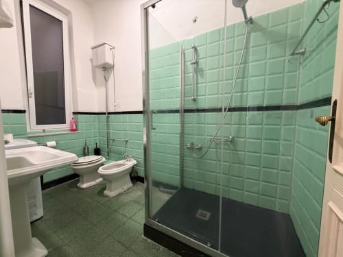 Bagno moderno nell'appartamento di Genova con piastrelle verde menta, doccia con box in vetro, WC, bidet e lavandino con specchio.