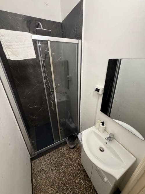 Bagno moderno nell'appartamento di Genova con doccia in marmo nero, lavabo bianco e pavimento in mosaico