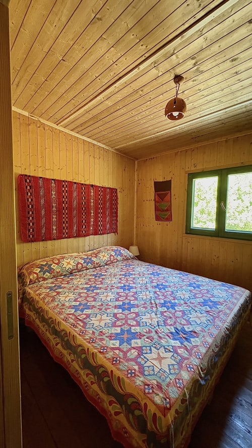 Camera da letto accogliente in legno al Podere di Maggio a Santa Fiora con biancheria a motivi, arazzi rossi e finestre verdi