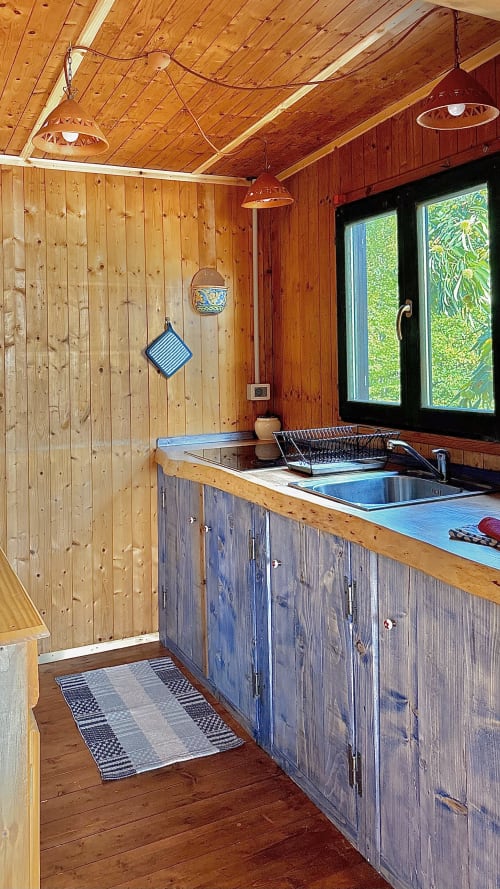 Cucina in legno con lavello in acciaio inox, pensili blu e ampie vetrate panoramiche sulla campagna di Podere di Maggio