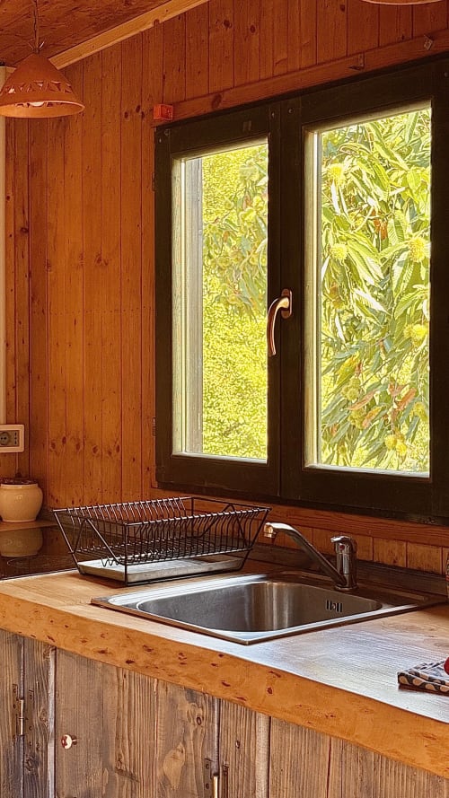 Lavello cucina in legno con vasca inox e rubinetto, gocciolatoio, finestre con vista sul rigoglioso giardino di Podere di Maggio