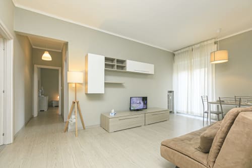 Moderno soggiorno genovese con divano beige, mobile TV in legno, zona pranzo e finestre panoramiche sulla città
