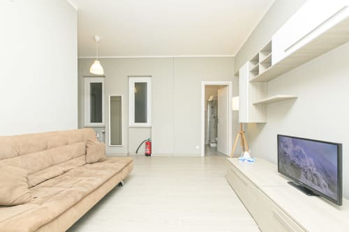 Soggiorno moderno in apartment EDERA HOUSE a Genova, con divano beige, TV schermo piatto, scaffali e vista sulla città