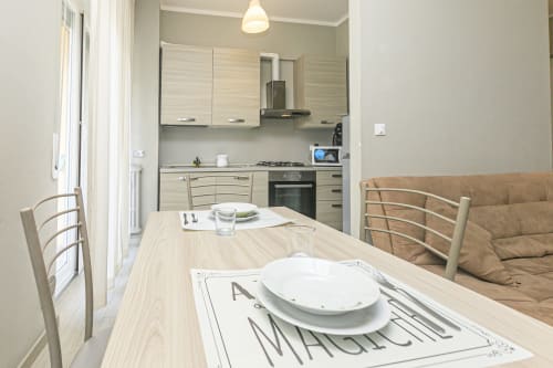Zona pranzo EDERA HOUSE con cucina nell'appartamento di Genova, con tavolo in legno, sedie, divano e elettrodomestici moderni