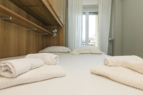 Moderna camera da letto nell'appartamento ML White House a Genova con letti rifatti, biancheria color crema, armadio in legno e balcone con vista sulla città