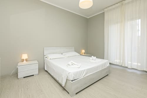 Camera luminosa nell'appartamento ML White House Genova con letto queen, comodini bianchi, lampade e tende trasparenti che si aprono su