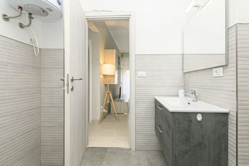 Bagno moderno nell'appartamento EDERA HOUSE a Genova, con mobile lavabo grigio, lavandino bianco e zona doccia piastrellata
