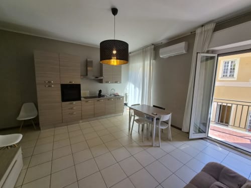 Moderna cucina open-plan e zona pranzo nell'appartamento di Genova con mobili in legno chiaro, illuminazione a sospensione e balcone con vista città