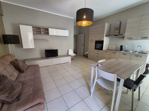 Moderno appartamento open-plan a Genova con cucina beige, tavolo da pranzo, divano marrone e lampada a sospensione nera