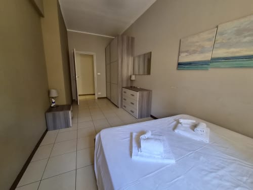 Ampia camera da letto nell'appartamento Vanilla House a Genova con letto bianco, guardaroba in legno e quadro con vista sulla città