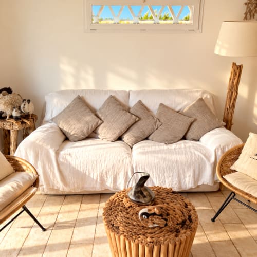 Salon lumineux de la villa aux Villas d'A Storia à Lecci, avec canapé crème, chaises en rotin et accents en bois naturel