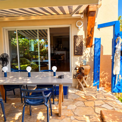 Terrasse ensoleillée des Villas d'A Storia à Lecci avec table à manger, chaises bleues, store rayé et portes vitrées