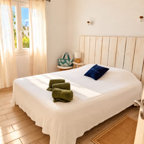 Chambre lumineuse aux Villas d'A Storia à Lecci avec literie blanche, tête de lit en bois, serviettes olive pliées et portes-fenêtres