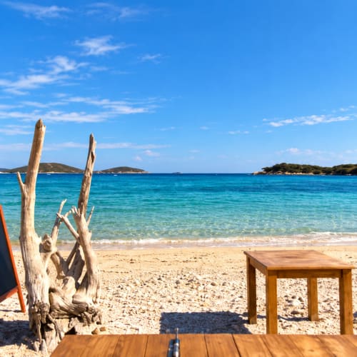 Vue sur la mer turquoise depuis la villa balnéaire Les Villas d'A Storia à Lecci, avec bois flotté et mobilier en bois