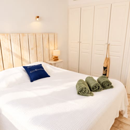 Chambre luxueuse aux Villas d'A Storia à Lecci avec lit blanc, tête de lit en bois, serviettes vertes roulées, coussin bleu marine