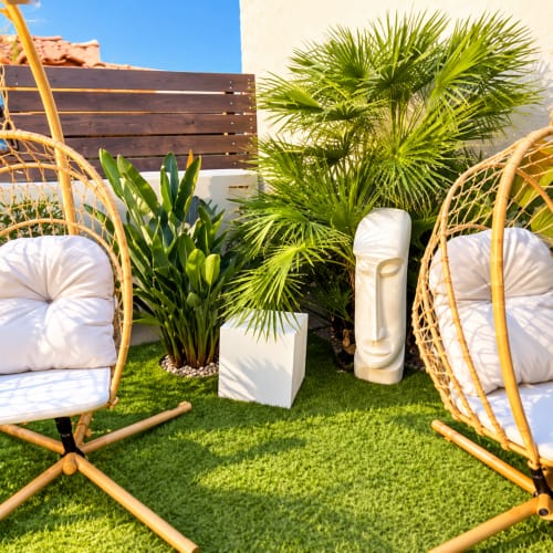 Espace de détente en plein air aux Villas d'A Storia avec chaises suspendues tissées, plantes tropicales et pelouse verdoyante à Lecci