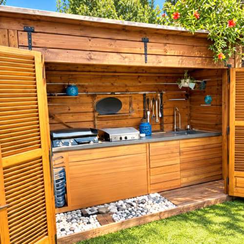 Pavillon de cuisine extérieure en bois avec plan de travail en acier inoxydable, grill intégré et accents bleus décoratifs aux Les