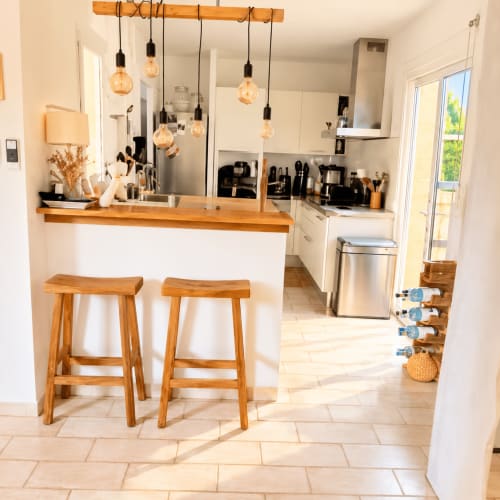 Cuisine moderne avec cabinetry blanc, tabourets bois, luminaires suspendus et électroménagers acier inoxydable aux Villas d'A
