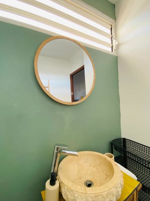 Salle de bain moderne de l'appartement Hibis Gold aux Maisons En Or avec miroir rond en bois et vasque crème sur mur vert