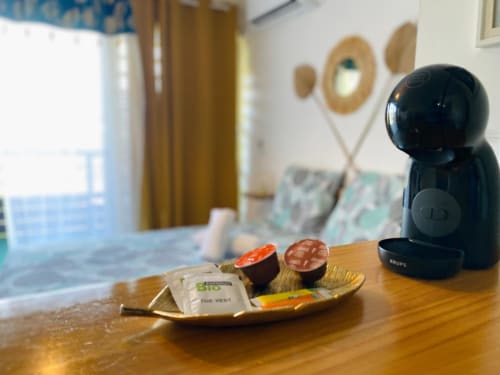 Cafetière noire avec sachets de thé et gourmandises sur un bureau en bois dans l'appartement Hibis Gold à Maisons En Or, Cayenne