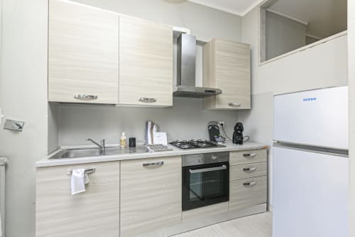 Moderna cucina genovese con mobili in legno chiaro, fornello a gas, cappa aspirante, lavello e frigorifero bianco