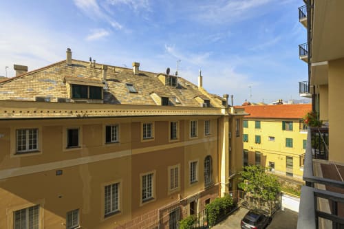 Affascinanti edifici europei gialli a Genova con vista sulla città, balconate e tetti in cotto sotto cielo azzurro