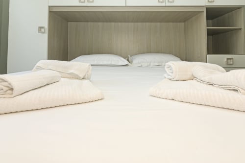 Due letti con biancheria bianca e coperte color crema ripiegate nella camera moderna con legno di ERICA HOUSE a Genova