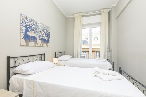 Camera luminosa dell'apartamento Erica House a Genova con due letti a struttura metallica nera, biancheria bianca, quadri blu e vista città