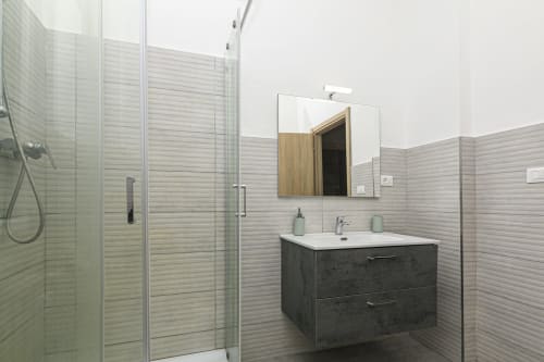 Bagno moderno dell'appartamento genovese con vanity scuro, lavabo bianco, piastrelle orizzontali, specchio con cornice in legno e vetro