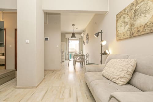 Soggiorno Papavero House Genova con divano beige, pavimenti in legno e balcone con vista sulla città