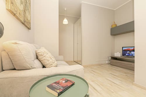 Elegante salotto moderno a Genova con divano beige, tavolo verde, TV e pavimenti in legno chiaro presso ML White House