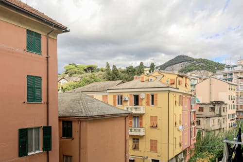 Edifici residenziali colorati nel centro di Genova con persiane verdi, sfondo montano e vista del cielo nuvoloso