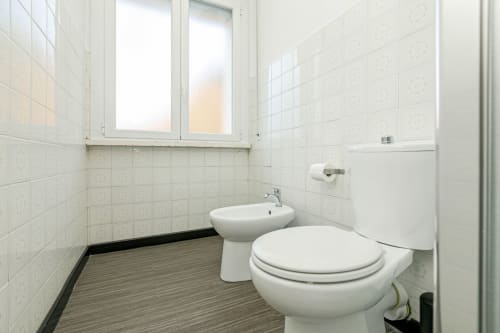 Bagno moderno nella Casa Papavero di Genova con piastrelle bianche, toilet, bidet e finestra satinata