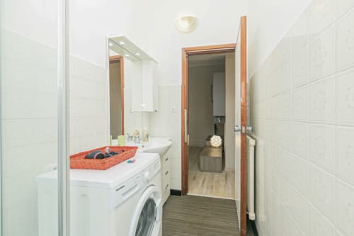 Bagno moderno con lavatrice, lavabo bianco, specchio e pavimento in legno ceramicato a Casa Papavero, Genova