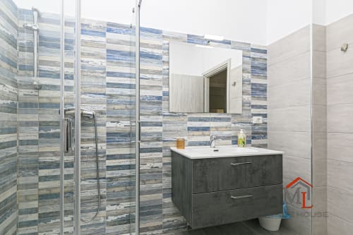 Bagno moderno nell'appartamento di Genova con piastrelle a righe blu, doccia walk-in, mobile scuro e specchio
