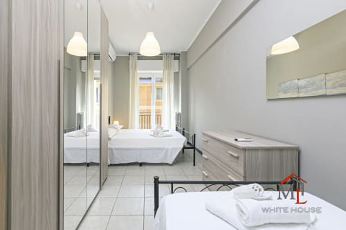 Camera da letto moderna a ML White House a Genova con armadio a specchio, biancheria bianca, luci a sospensione e balcone con vista città